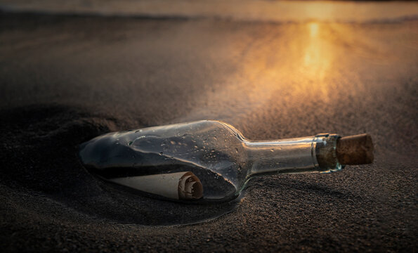 Glass bottle with message inside on beach at sunset