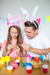 Father and his little daughter painting eggs. Happy family preparing for Easter.