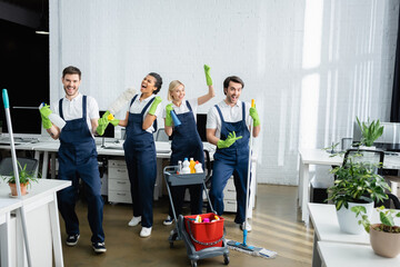 Excited multiethnic cleaners in uniform looking at camera in office