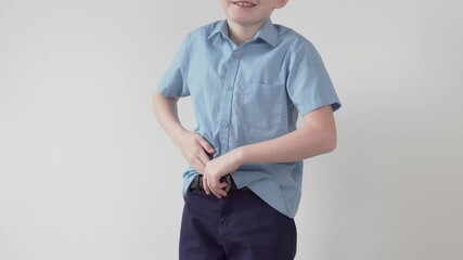 A beautiful blonde boy tucks his shirt into his trousers. A schoolboy wears a school uniform.