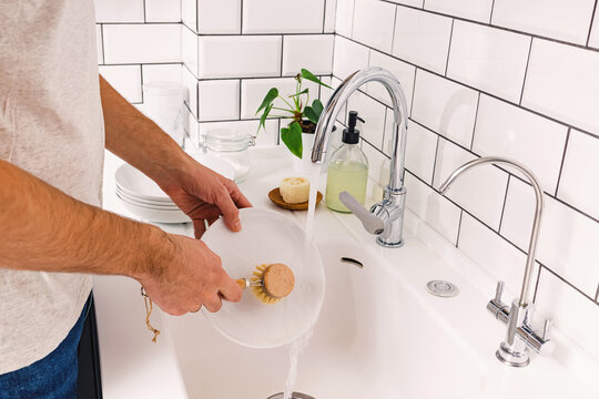 A man washes dishes in the kitchen with a wooden eco brush