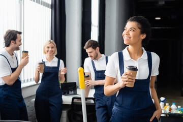 African american cleaner with takeaway drink standing near colleagues talking in office