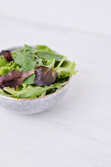 green healthy salad with arugula in clay bowl standing on the white table copy space
