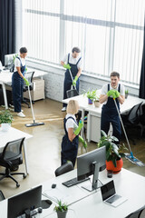 High angle view of multiethnic cleaners washing floor near computers in office