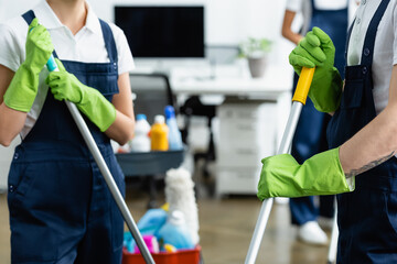 Cropped view of cleaners in rubber globes holding mops in office