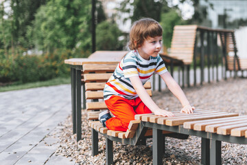 A beautiful child kid boy sits on the wooden playground and in the summer. Cute Schoolboy playing outdoors.