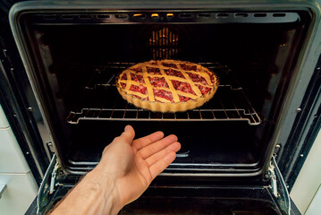 Human hand loading lingonberry pie pan into oven on baking plate