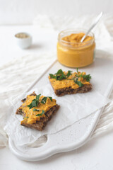 Crispy crispbreads with hummus and herbs on a white cutting board, hummus in a glass jar