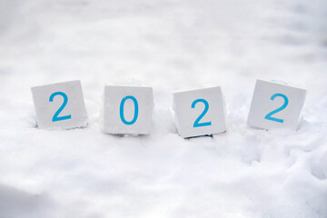 Wooden cubes with year 2022 on a white snow background. New Year and Christmas concept. 