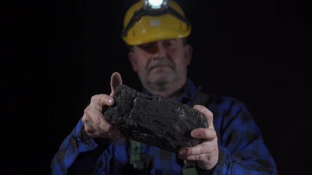 A miner turns a large lump of black coal in his hands. Close-up view