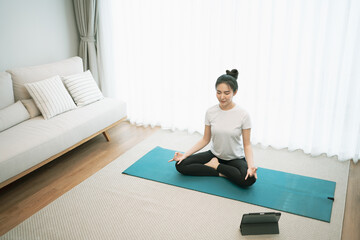 Fototapeta premium Portrait of gorgeous young asian woman practicing yoga at home stretching out while following a yoga routine.
