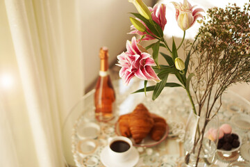 Bouquet of lilies. Cup of coffee, croissants and wine - blurred background.