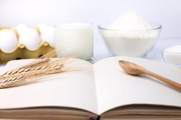 Blank recipe book and baking ingredients: flour, eggs, milk and sugar. Cooking process. Close-up.