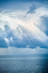 Sunbeam rays shining through the clouds on blue sky over the ocean