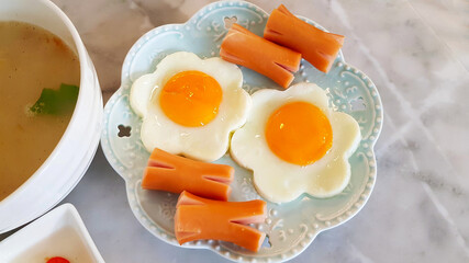 Morning breakfast with Flower-shaped fried egg and sliced sausage on dish or plate with boiled rice in Thai style on marble table and copy space. Close up food 