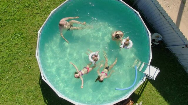 A group of children is having fun in the blue round swimming pool in the backyard. Aerial shooting of backyard swimming pool