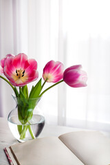 Bouquet of pink tulips in vase and open book lie on the table. Selective focus.