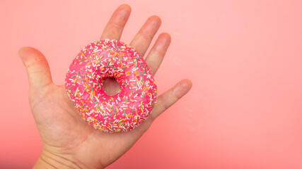 Red donut in hand on a pink background.