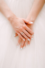 Graceful hands of the bride folded on a fluffy skirt of a wedding dress, close-up 