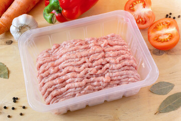Raw minced meat in plastic container with vegetables and spices on wooden background