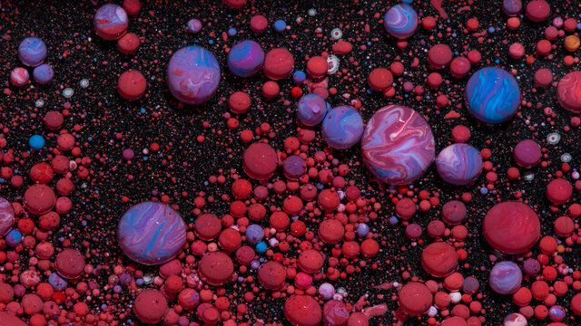 Abstract background of bobbly mixed pink and blue oil-based paints on a dark surface