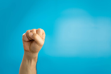 Male clenched fist, isolated on a blue background. Fist held tightly against blue pastel...