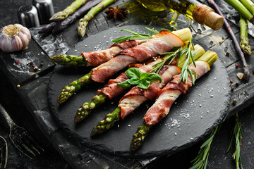 Baked asparagus with bacon and spices on a black stone plate. Top view. Free space for your text.