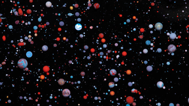 Abstract background of bobbly mixed pink, orange, and blue oil-based paints on a dark surface