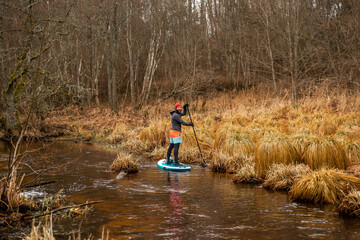 Fototapeta na wymiar Young men paddle with SUP or stand up paddle board in small river. concept of harmony with the nature. Stand up paddle boarding - awesome active outdoor recreation.