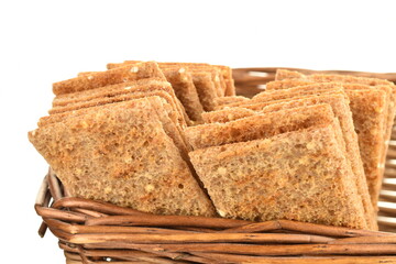 Several multigrain thin crisps in a basket of vine, close-up, isolated on white.