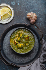 Traditional Indian Punjabi food Palak Paneer with spinach and cheese in vintage metal bowl with spoon on rustic concrete background from above 