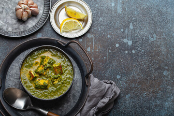 Traditional Indian Punjabi food Palak Paneer with spinach and cheese in vintage metal bowl with spoon on rustic concrete background from above with space for text
