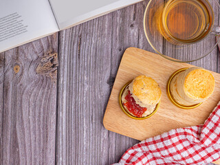 Top view of scones traditional English delicious fresh bake homemade, strawberry jam placed on a plate with a cloth and a teacup on vintage background. Dessert, beverage, and relaxation concept