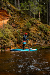 Fototapeta na wymiar Young men paddle with SUP or stand up paddle board in small river or national park and explore nature. concept of harmony with the nature. Stand up paddle boarding - awesome active outdoor recreation.