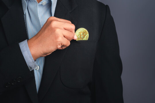 An investor guy holding a bitcoin golden coin put to suit pocket with a gray background. Close-up photo. Space for text. Virtual cryptocurrency and future money concept