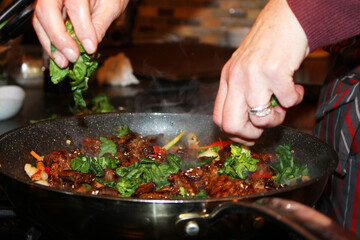 Close-up of  woman's hands adding Bok choy to a Korean beef stir-fry, Bulgogi