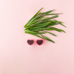 Face with heart-shaped sunglasses and hair made of green fresh leaves on pastel pink background. Minimal vacation concept.