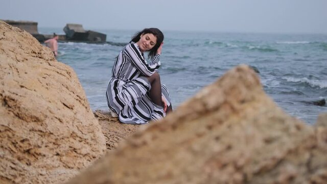 Summer lifestyle fashion image of happy stunning woman sitting on cliff ocean.