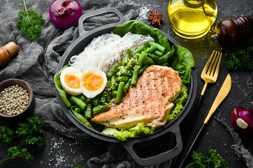 Baked chicken fillet with rice pasta, spinach and beans in a black stone plate. Dietary food. Top view. Free space for text.