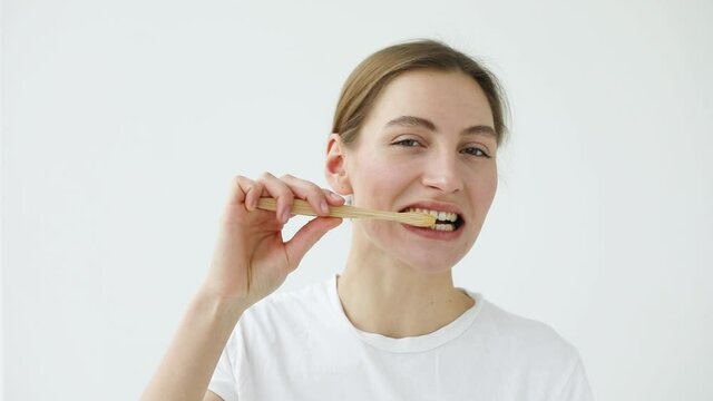 a beautiful girl of European appearance in a light T-shirt brushes her teeth at the camera, as in a mirror
