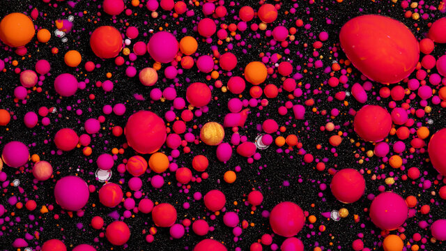 Abstract background of bobbly mixed pink, orange, and dark oil-based paints on a dark surface