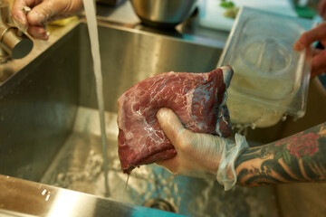 Close up of hands of male cook cleaning the raw pork under tap water for cooking