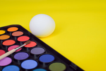 Easter painting of eggs. The set of paints lies on a yellow background. A white egg for Easter traditions.