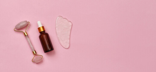 Rose quartz gua sha stone, jade roller and glass eye dropper serum bottle isolated on pink surface