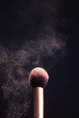 Makeup brush with a highlighter that effectively spreads in different directions. Dark background, minimalism, copy space. Make-up, cosmetics, visage concept.
