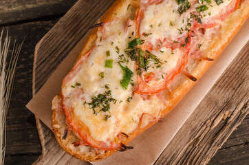 Loaf stuffed with cheese and tomatoes close up on wooden background, fast food