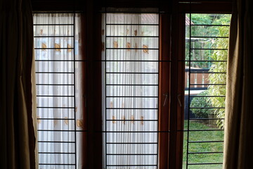 Light curtains on a window, one part of which is open, showing a garden view on the outside 
