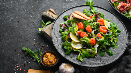 Fresh salad with salmon and olives in black plate. Top view. Free space for your text. Rustic style.