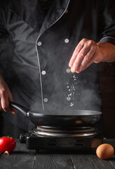 The chef adds salt while cooking eggs in pan. Work environment on vintage kitchen table. Vertical...