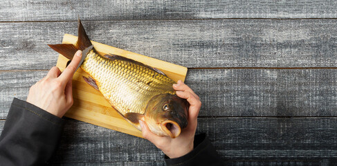 Cooking. cleaning fresh carp. Chef's hands brushing fresh fish on wooden cutting board on black...